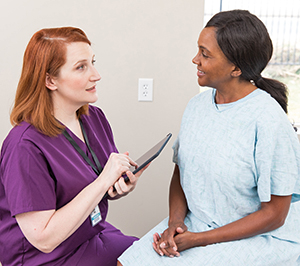 Healthcare provider with digital tablet talking to woman in exam room.