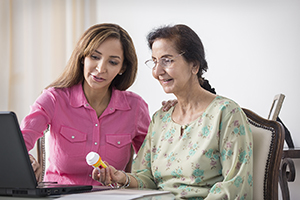 Two women looking at medication bottle and laptop.