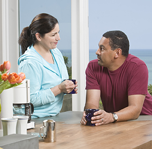 Man and woman talking over coffee at kitchen counter.