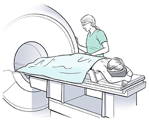 Woman lying face down on scanner table; healthcare provider preparing her for breast MRI.