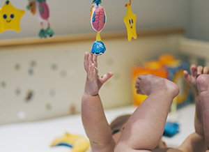 Baby lying in a crib reaching up to a mobile.