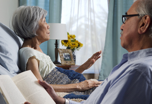 Woman sitting up in bed, man sitting nearby.