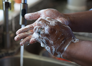 Closeup of hands in sink with running water. Hands are covered with soap suds.