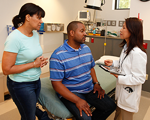 Man and woman talking to healthcare provider in exam room.