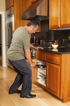Man bending at knees to retrieve a pan from a lower cabinet.