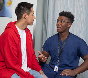 Healthcare provider talking to teen boy in exam room.