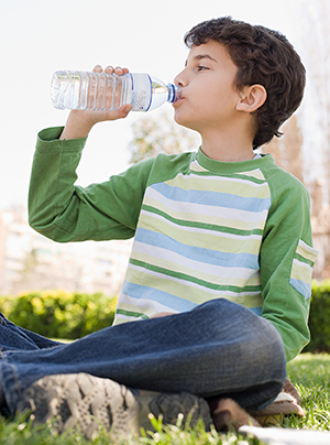 Boy drinking water from bottle sitting on grass outdoors.