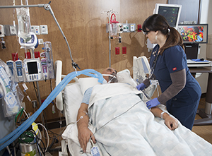 Healthcare provider caring for intubated patient in intensive care unit.