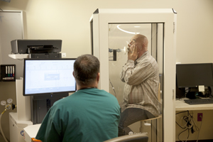 Technician performing pulmonary function tests on man in testing booth.